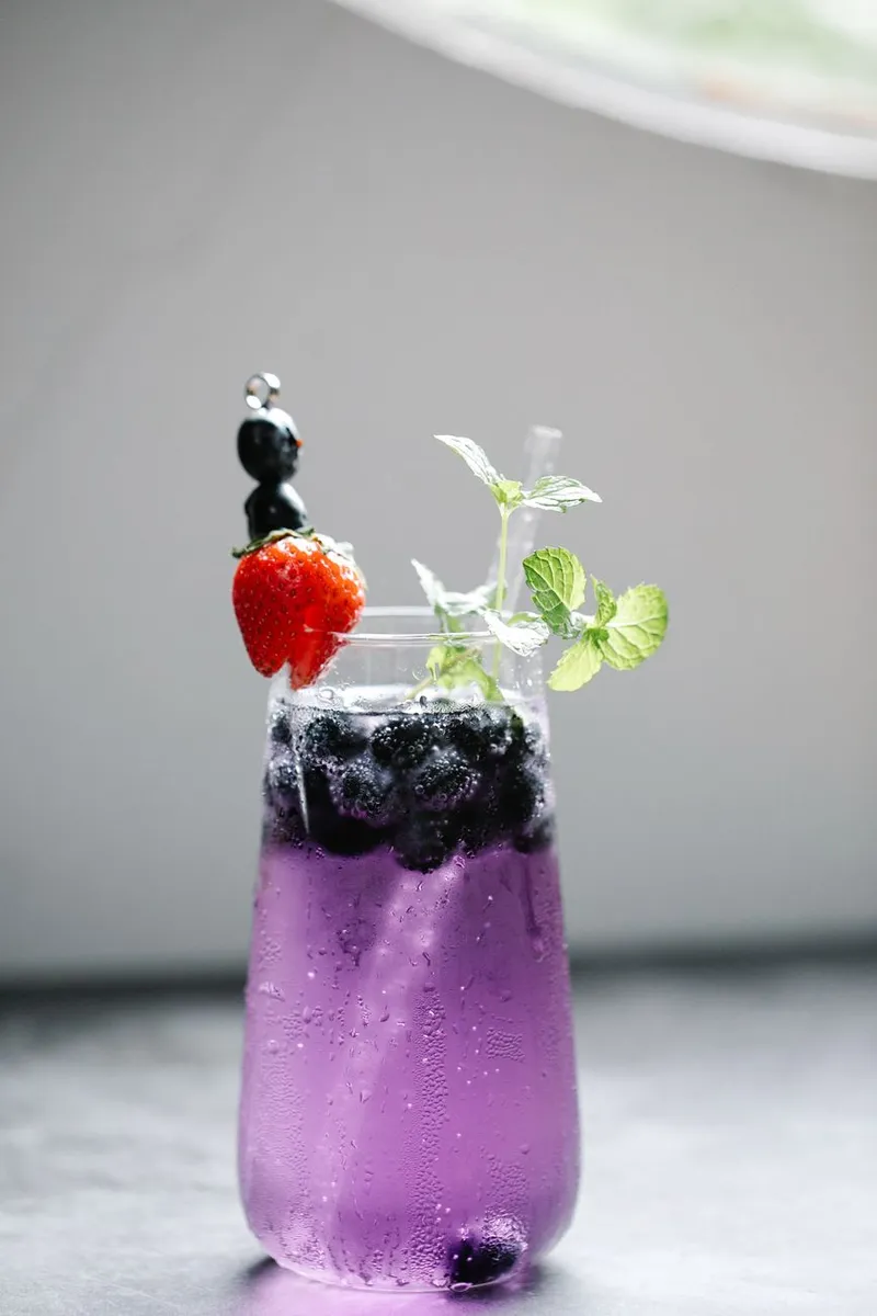 Vibrant purple cocktail garnished with berries and fresh mint in a glass.