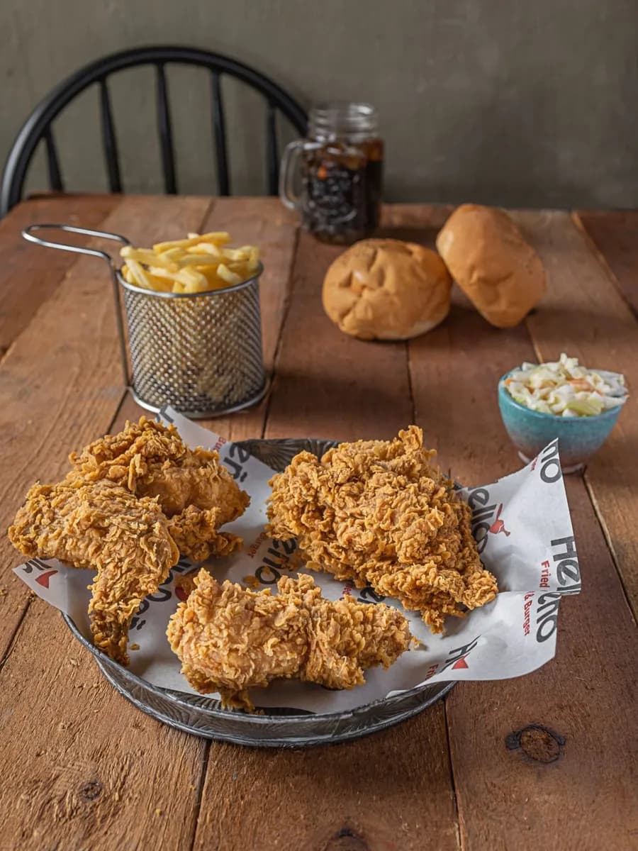 Crispy fried chicken served with fries, buns, and coleslaw on a rustic wooden table.