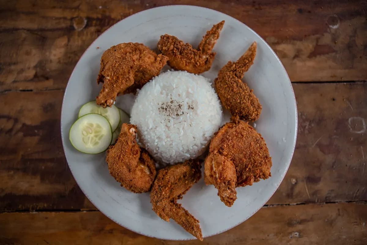 Top view of appetizing golden chicken wings with cooked rice and cucumber slices on wooden table